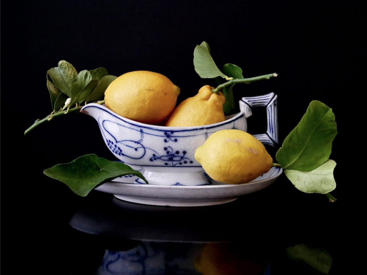 A vibrant, minimalist still life of three lemons against a teal background.